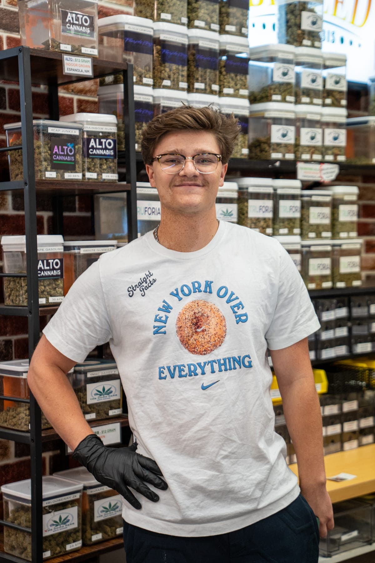 Van, one of our budtenders, standing in front of the wall of flower jars, gloves on
