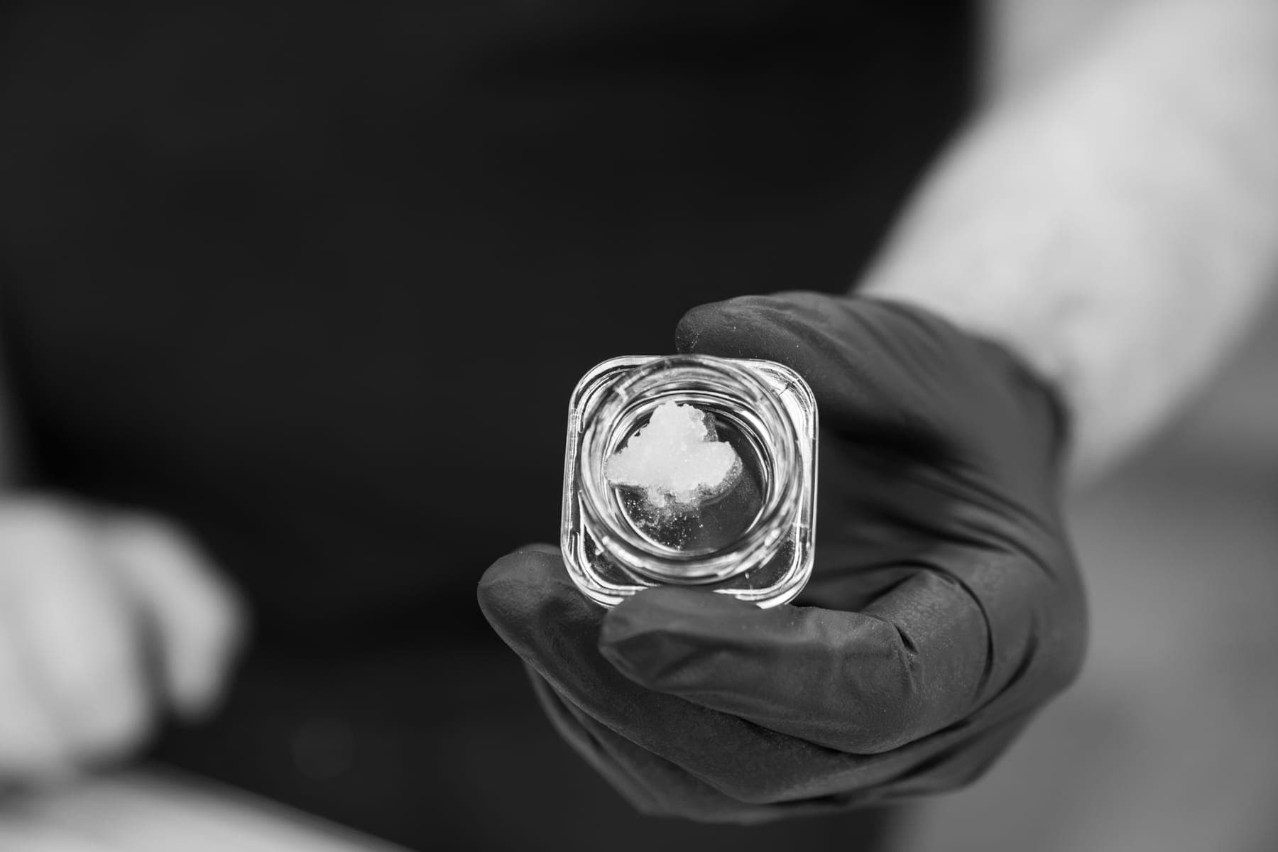 Black-and-white photo of a jar of concentrate in a gloved hand