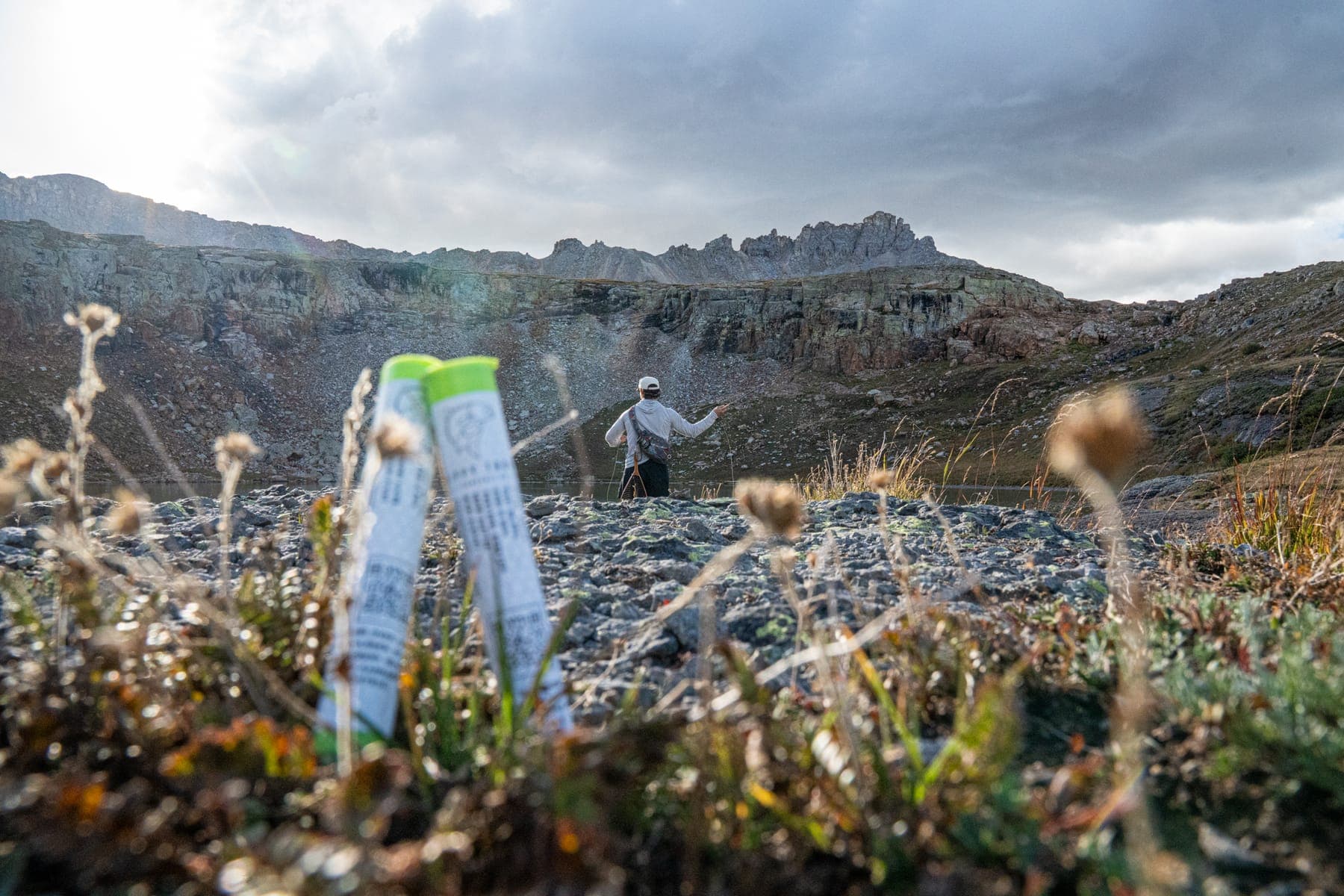 Two pre-roll tubes standing in the wildflowers, an angler on the ridge behind them