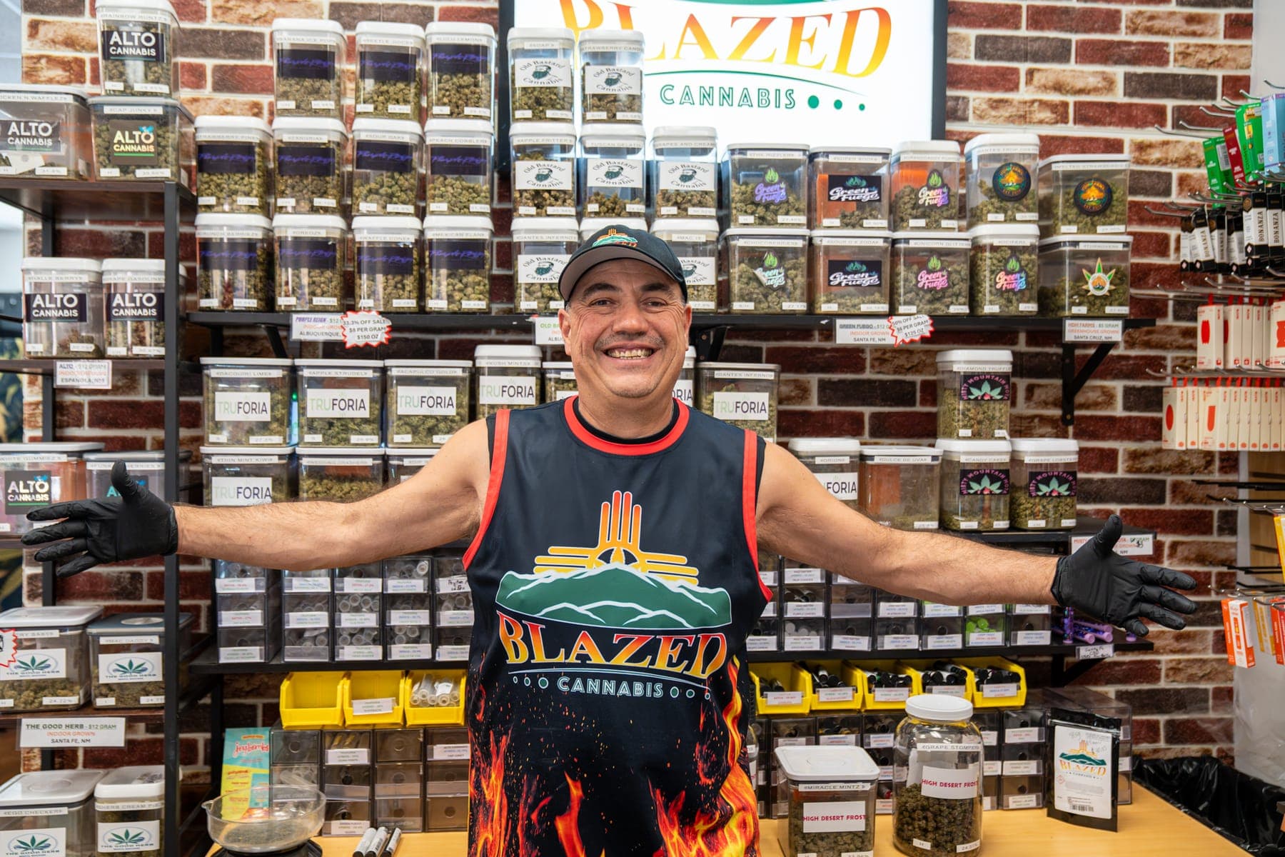 James, one of the owners, with his arms spread wide in front of the wall of flower jars
