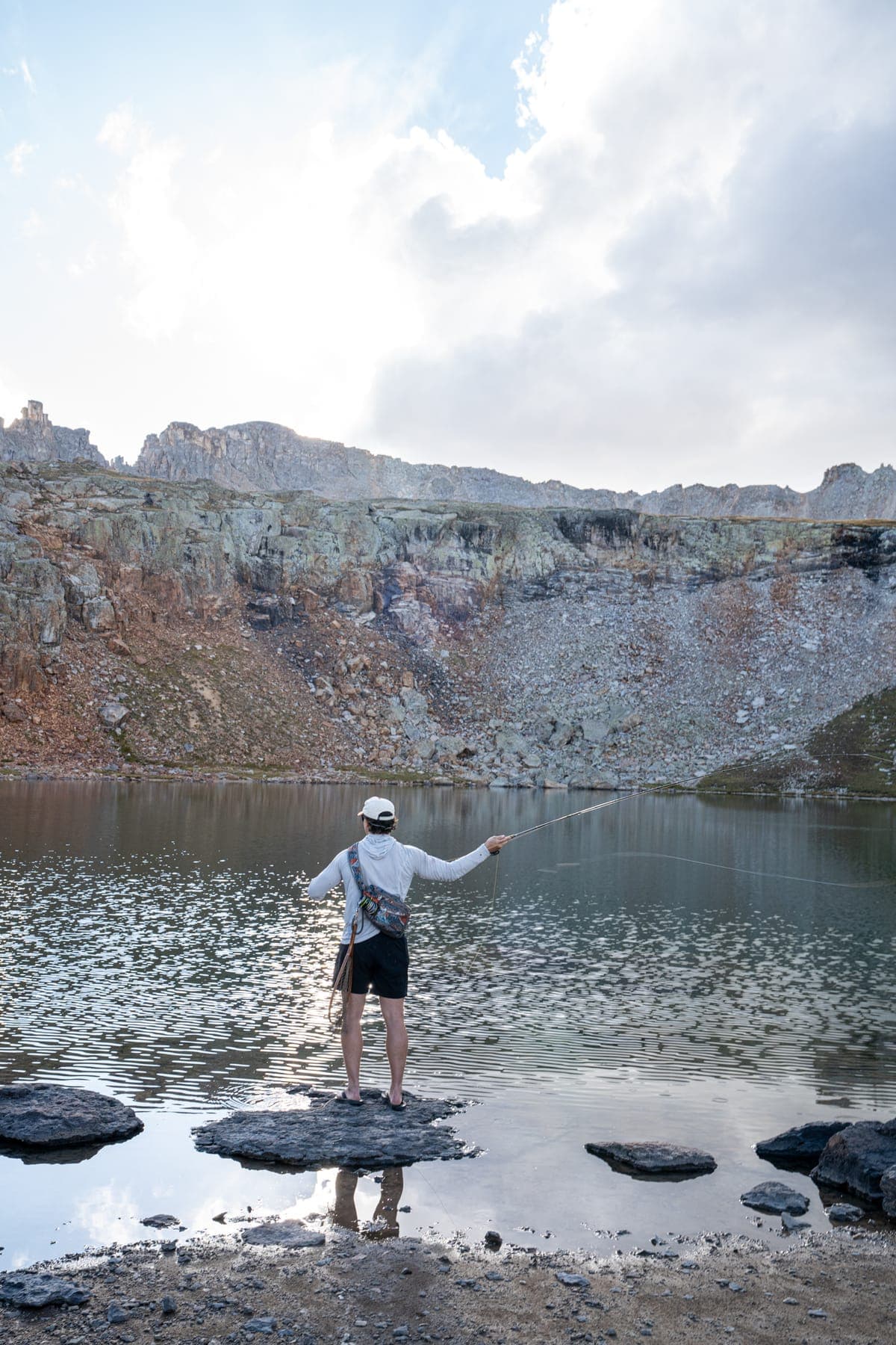 Fishing from the rocks at the edge of an alpine lake under a big sky