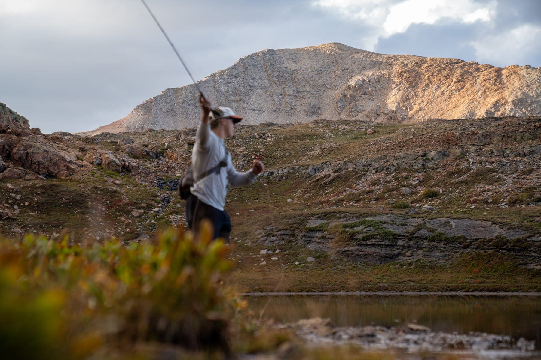 Mid-cast from the bank, a bare peak across the lake