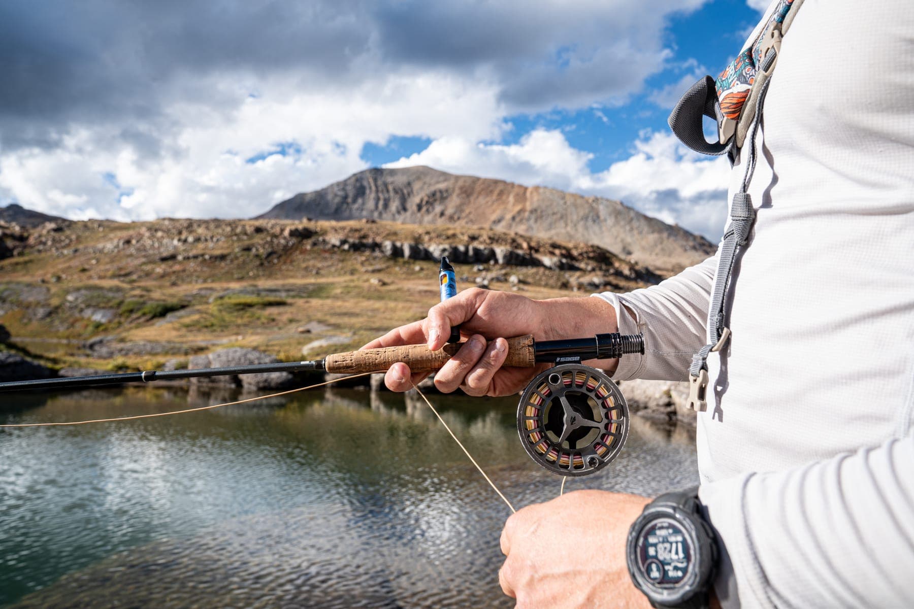 Close-up of a fly reel in hand, the lake and clouds behind