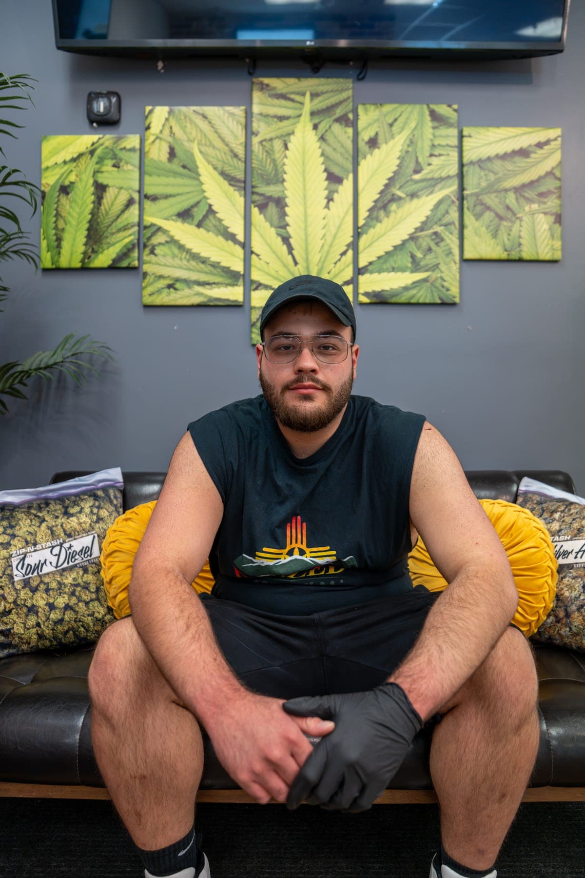 One of the sons sitting on the shop couch beneath the cannabis-leaf canvas