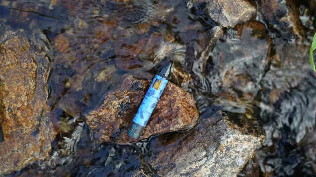 A vape pen resting on a wet rock in a mountain stream